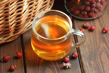 Rosehip brewed tea in a glass cup with red berry near on wooden rustic table, natural remedy and support for heart disease, diabetes, immune health, closeup, copy space, naturopathy, medicine concept