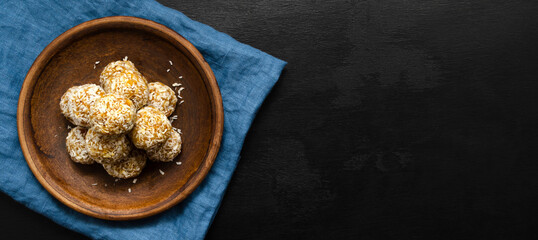 banner home made nutritious energy balls consisting of nuts, oatmeal, honey, dried fruits on a clay plate on a dark black slate background with a blue towel with place for text. healthy snack