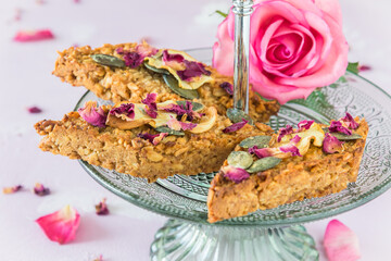 Homemade apple muesli bars with pumpkin seeds and rose petals on a light green glass cake stand on a delicate pink background
