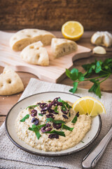 Arabian cuisine: Baba Ganoush with black olives and minced parsley and flatbread on a rustic wooden table. Vertical.