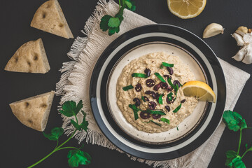 Arabian cuisine: Baba Ganoush with black olives and minced parsley and flatbread on a black background, top view