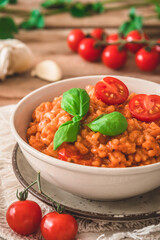 Homemade tomato risotto with fresh basil on a rustic wooden table, vertical