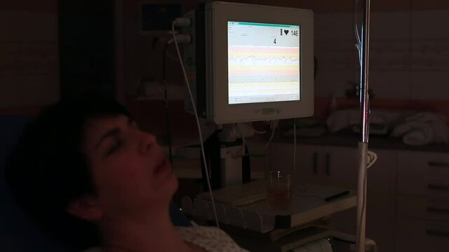 The monitor shows the patient's heartbeat. The woman is in the hospital. Health analysis. Dark background.