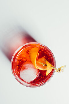 Glass of bitter alcoholic Negroni cocktail served with ice and orange peel on white surface
