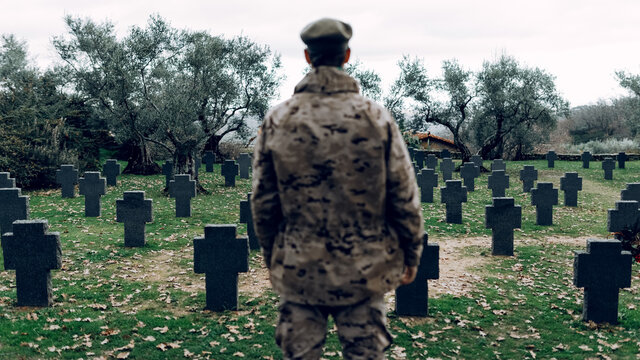 Back view anonymous soldier wearing camouflage outfit standing on vast military cemetery on early autumn day