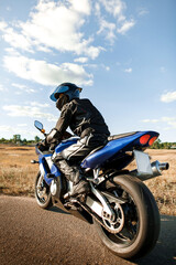 Biker or motorcyclist in a black leather suit and helmet sits on a sports motorcycle and looks into the distance. Vertical photo orientation