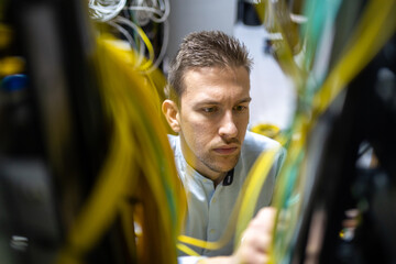 Concentrated male specialists working with wires in server while managing network in data center