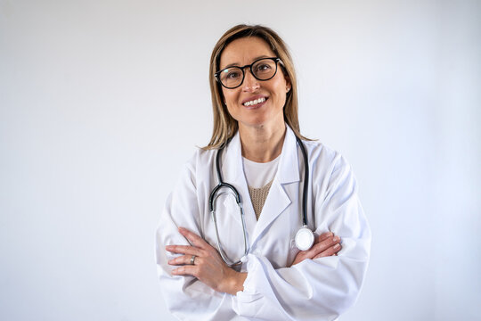 Smiling female medic wearing white uniform standing with stethoscope and arms crossed in hospital and looking at camera