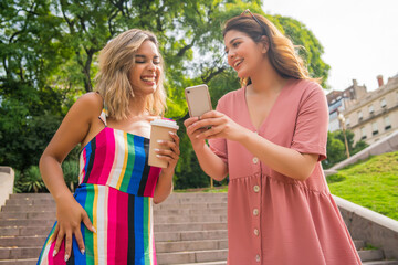 Fototapeta premium Two friends using mobile phone outdoors.