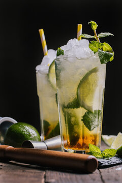Glasses with cold alcohol Mojito cocktail with rum and fresh lime served with ice and mint leaves on wooden table with squeezer and jigger