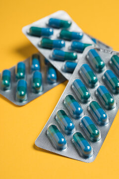 From above of plastic blister packs with blue medical capsules placed on yellow background