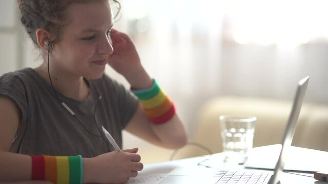Curly-haired teenager girl makes homework near the laptop. Online learning, distance learning, home schooling