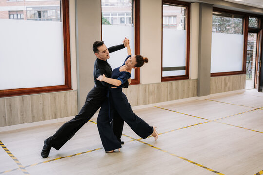 Skilled couple of dancers in elegant clothes rehearsing moves of ballroom dance during class in studio