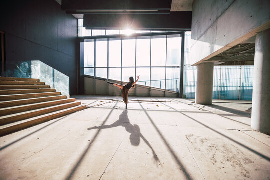 Side view of unrecognizable female theater artist dancing with raised leg and arm on floor with shadow against glass wall