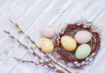 colorful easter eggs in a nest and blossoming willow twigs on a white board table