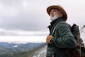 Side view of elderly male traveler with backpack standing in highlands in winter and admiring scenic landscape in Caceres