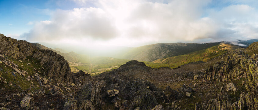 Picturesque panoramic view of high ridges under glowing blue sky with clouds in sunlight