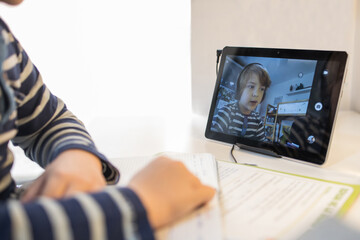 Schoolkid in headphones talking on video chat on tablet while sitting at table at home and having online lesson