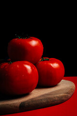 Group of ripe red tomatoes on wooden board with black background. Vegan concept. Vegetables.