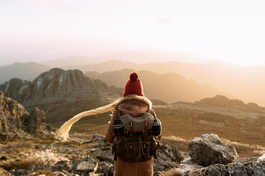 Back view of unrecognizable hiker standing on stone and observing amazing scenery of highlands valley on sunny day