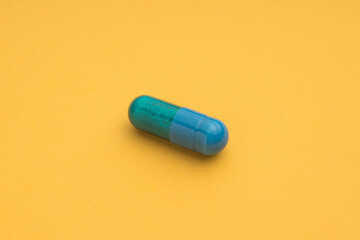 High angle of blue capsule of pharmaceutical medicinal product placed on bright yellow background