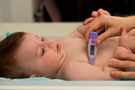 Crop loving mother measuring temperature of cute baby and placing thermometer in baby underarm carefully