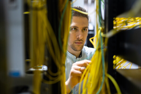 Concentrated male specialists working with wires in server while managing network in data center