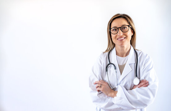 Smiling female medic wearing white uniform standing with stethoscope and arms crossed in hospital and looking at camera
