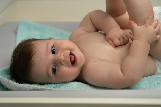 Cheerful little baby in diaper lying with legs raised on changing table and looking away happily