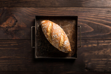 Top view of appetizing crispy freshly baked bread loaf with golden crust on metal tray placed on wooden table