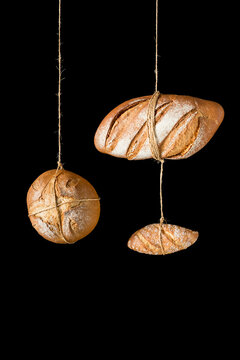 Loafs and pieces of fresh artisan crispy bread of various shapes and sizes hanging on ropes against black background