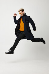 a man jumped and runs to the side on a light background in a coat, trousers and boots