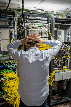 Back view of unrecognizable male technician grabbing head while having problem in data center with server racks