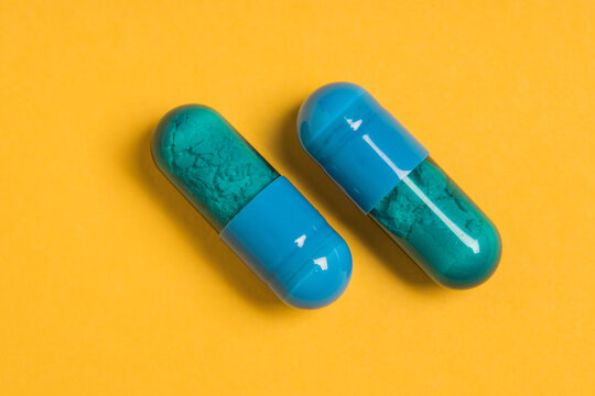 High angle of blue capsules of pharmaceutical medicinal product placed on bright yellow background