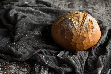 From above of appetizing freshly baked whole round bread loaf arranged near wooden spoon on gray cloth sprinkled with flour