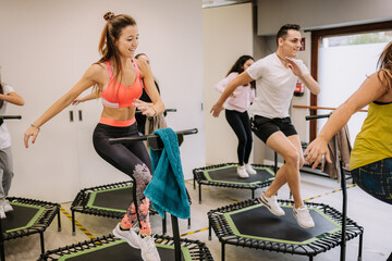Company of sportspeople jumping on trampolines with raised arms during active fitness training in gym