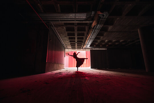 Anonymous female dancer in dress dancing with raised arms and leg on theater stage during rehearsal
