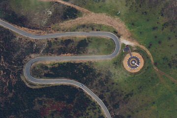 Spectacular drone view of curved serpent road near round concrete helipad on grassy rural valley on summer day running through green hills in highlands