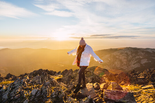 Anonymous female tourist in outerwear strolling on rough stones in mountains under cloudy sky at shiny dawn in back lit