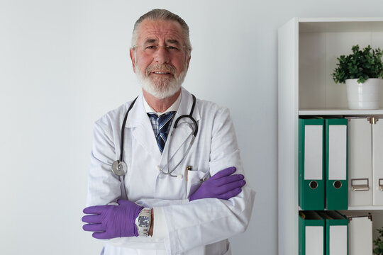 Physician in robe with stethoscope putting on sterile gloves in clinic in daytime