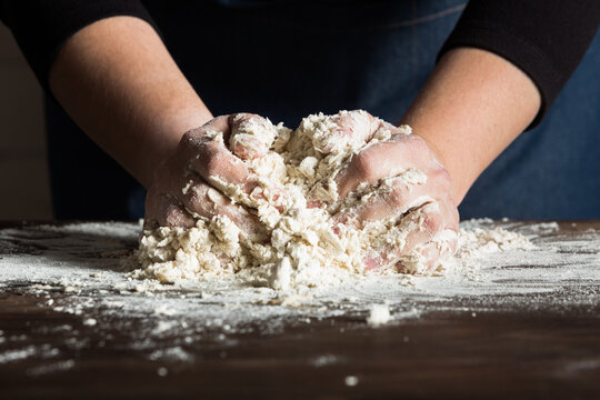 Crop anonymous baker kneading dough on table with flour while preparing bread in bakery
