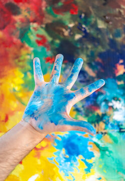 Artist with open hand showing palm with blue paint near colorful canvas in studio