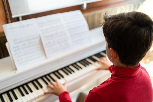 From above back view of anonymous child playing piano while reading notes and rehearsing song at home
