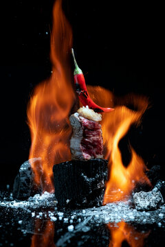 Delicious beef meat fillet placed on charcoal piece and preparing on flame against black background