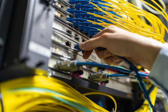 From below of crop anonymous man putting electronic cable in data system in communications room