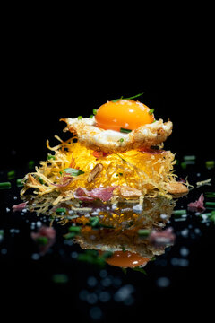Appetizing crispy potato hash brown nest with egg yolk served on mirrored surface against black background