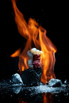 Delicious beef meat fillet placed on charcoal piece and preparing on flame against black background