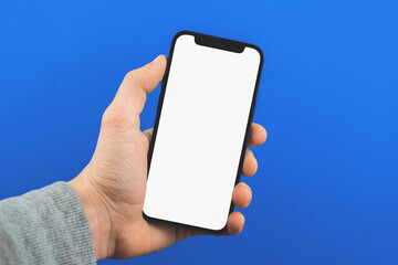 Mockup with male hand holds smartphone with blank white screen on blue background
