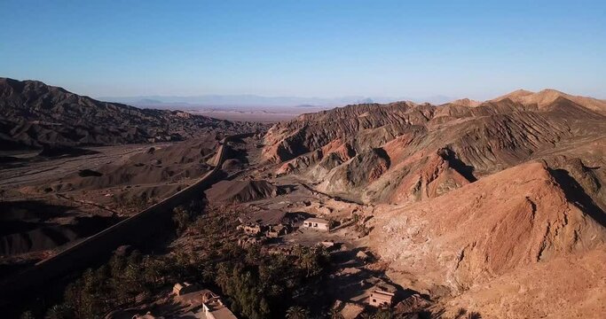 Ruins of Abandoned Mudbrick Adobe House Buildings in the Middle of Desert in Ardakan Yazd Iran Middle East Asia - Aerial Move Up Shot and Sand Dunes Visible in Background and Date Palm Tree in Town