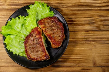 Poster Grilled pork steaks with lettuce leaves on wooden table. Top view © olyasolodenko